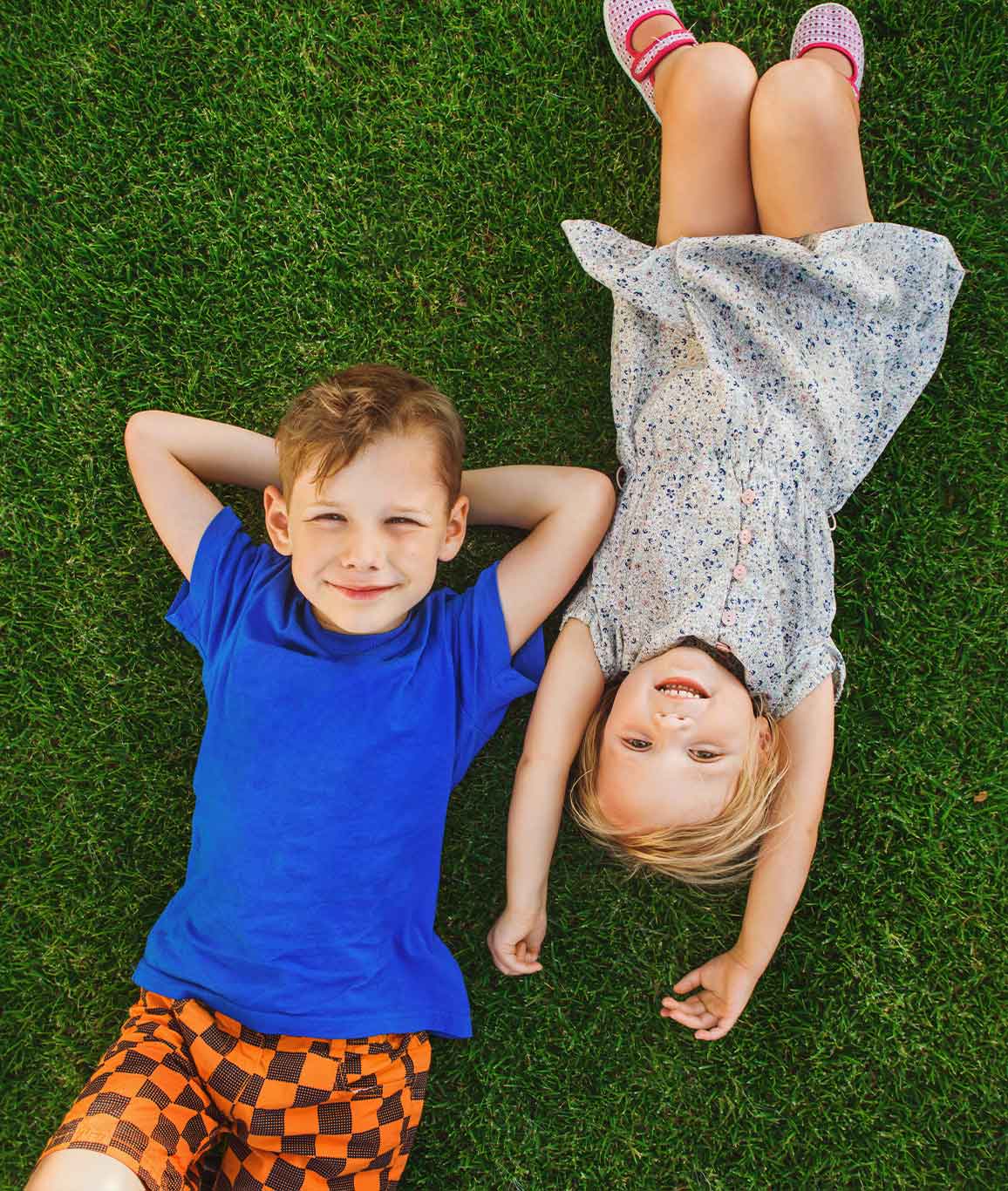 Two young kids lying on a lawn looking up and camera center