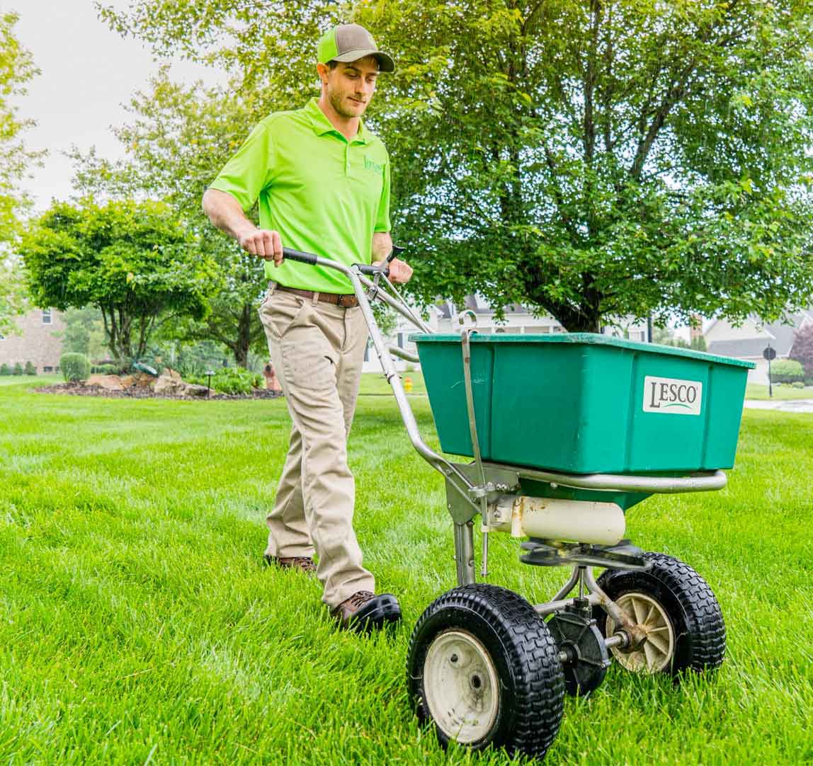 Green group employee pushing a cart across a lawn to spread fertilizer