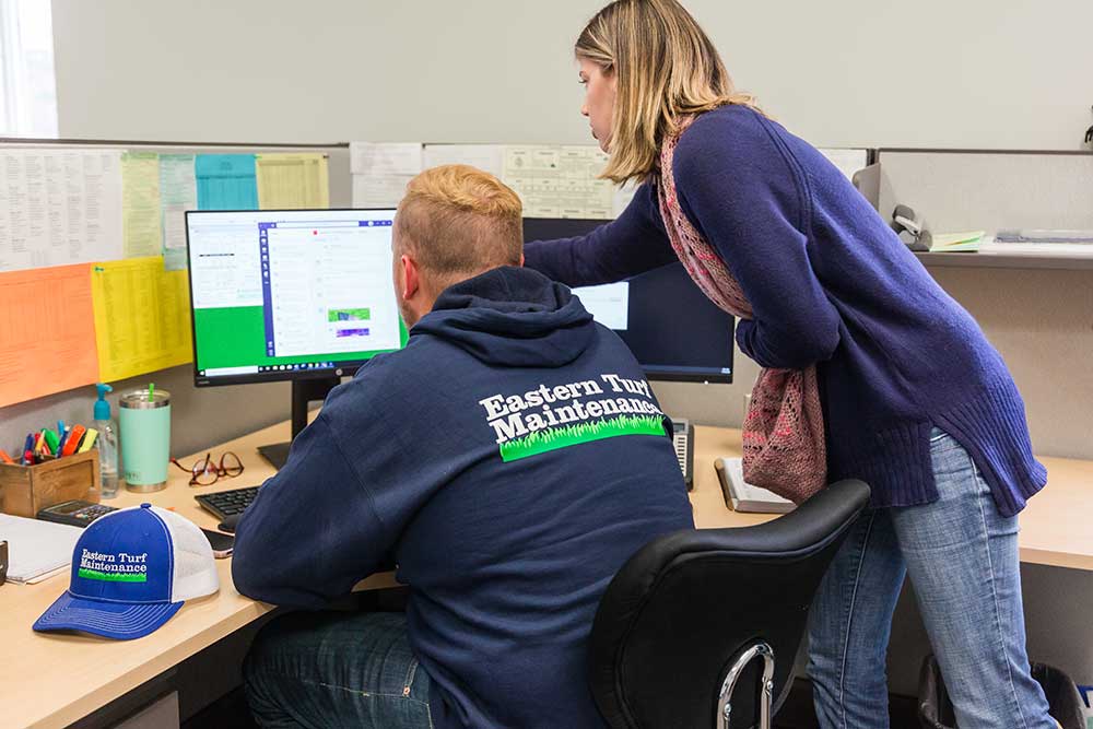 Two green group employees looking at a computer screen