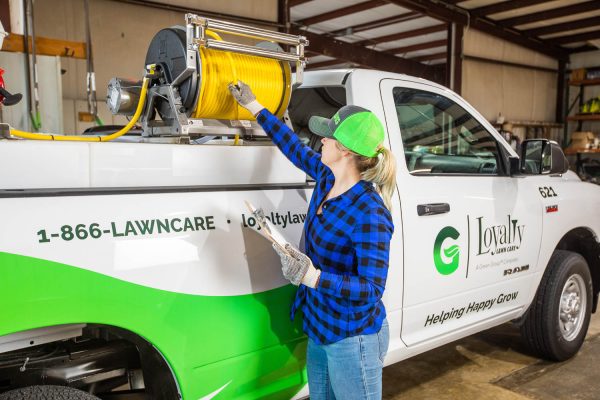 A woman checking a hose on the back of a lawncare truck